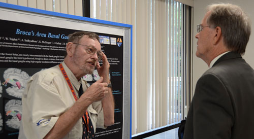 An investigator explaining research results to a man as they stand in front of a poster displaying information about the research