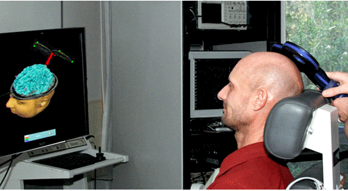 Man undergoing transcranial electrical stimulation while looking at image of brain on computer monitor